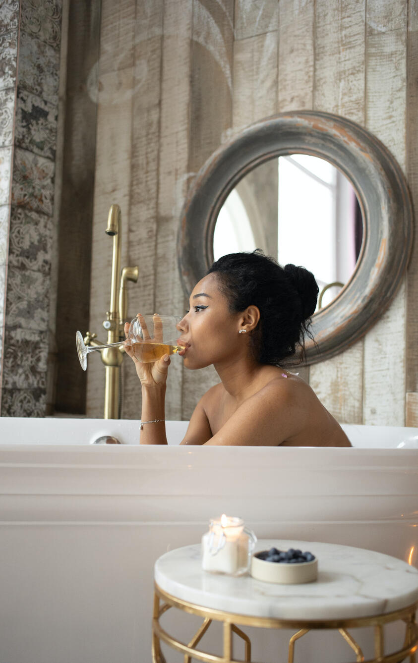 Woman enjoying her self-care moments, drinking wine in a bathtub